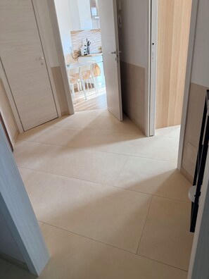 A hallway with a kitchen area visible in the background, featuring a dining table and chairs.