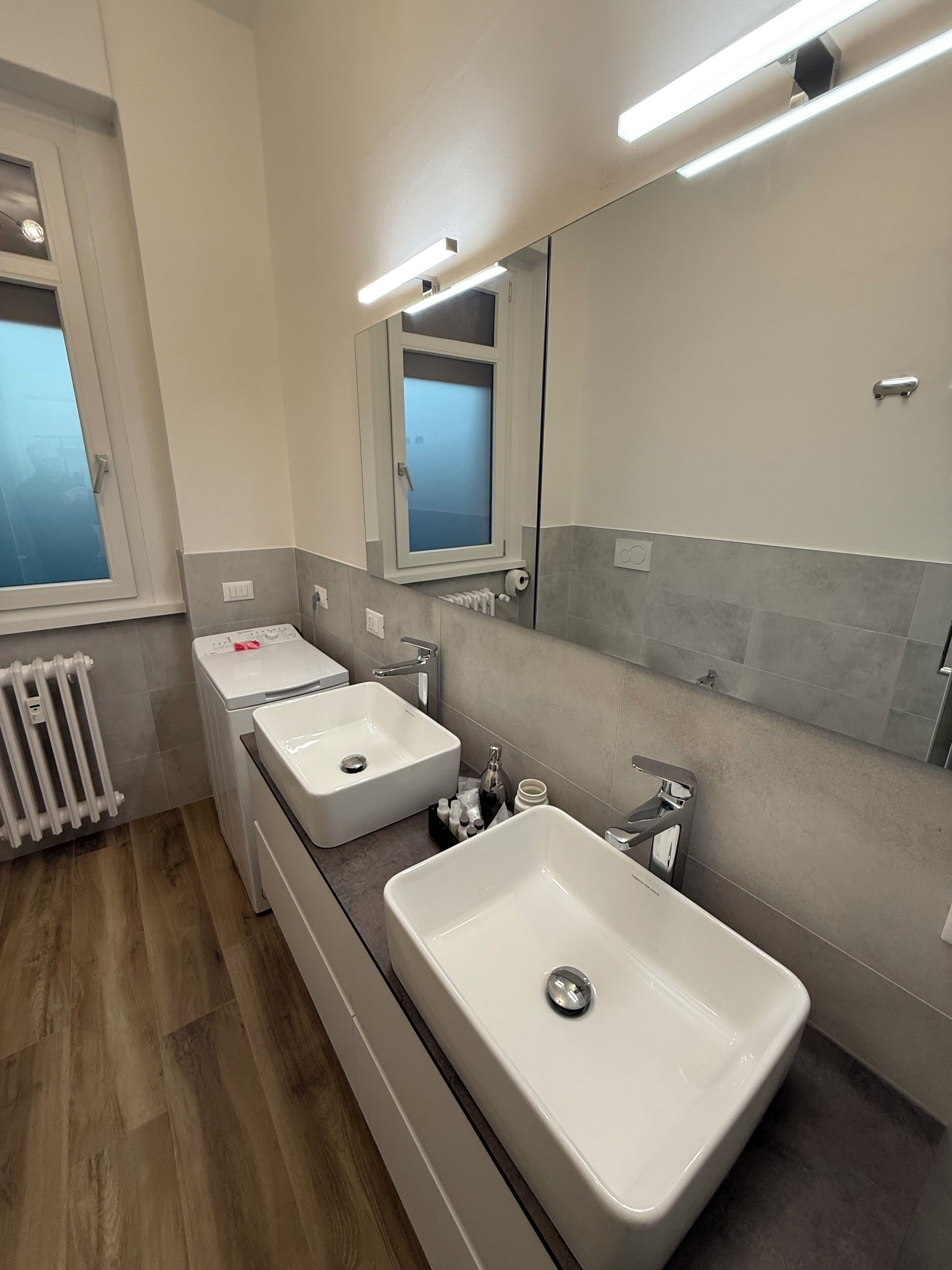 A modern bathroom with two sinks, a large mirror, and a window.