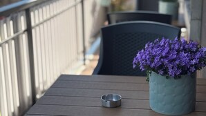 Una mesa de madera con un cenicero de metal y una planta en maceta con flores moradas en un balcón.
