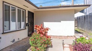 A single-story house with a front door, a small porch, and a garden with various plants. - Cute Pacific Beach Unit! Walk to the Beach! (San Diego)