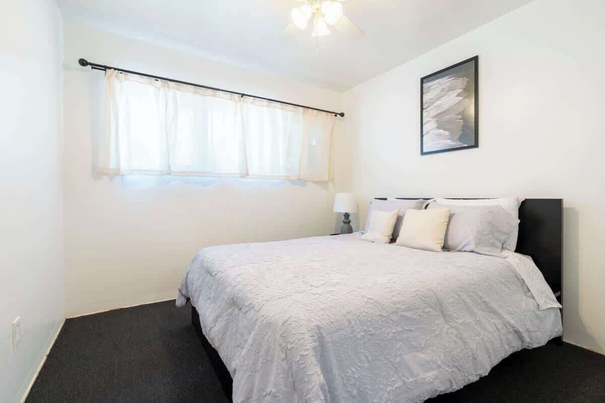 Une chambre à coucher avec un lit, une fenêtre avec des rideaux, un luminaire fixé au mur et un tableau encadré.