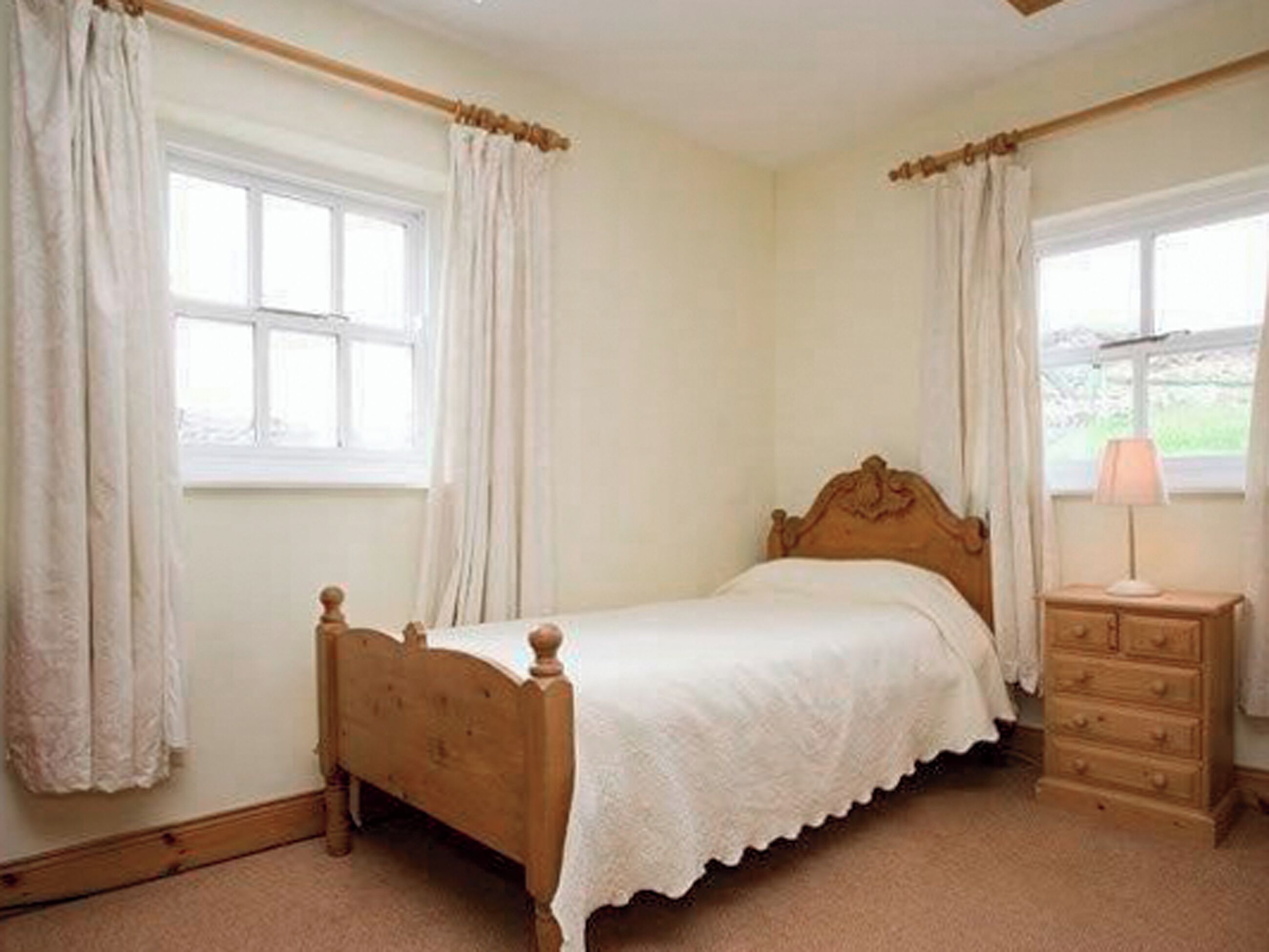 A bedroom with a wooden bed, a nightstand, and a window with curtains.
