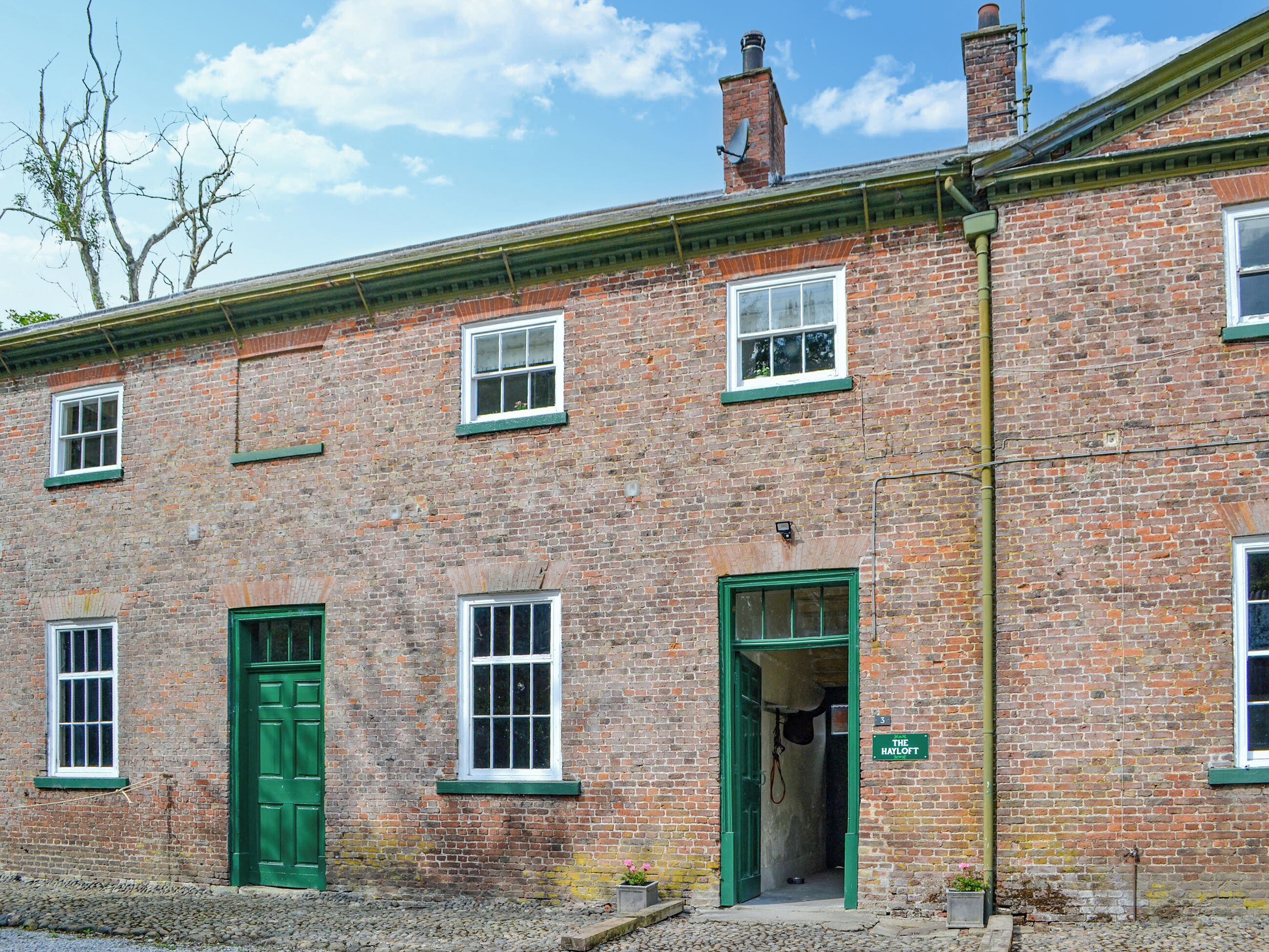 A brick building with green doors and windows, a chimney, and a sign indicating 'The Hayloft.'