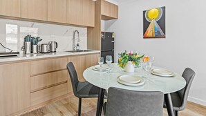 Eine moderne Küche mit Holzschränken, einer weißen Arbeitsplatte und einem Essbereich mit rundem Tisch und vier Stühlen.
