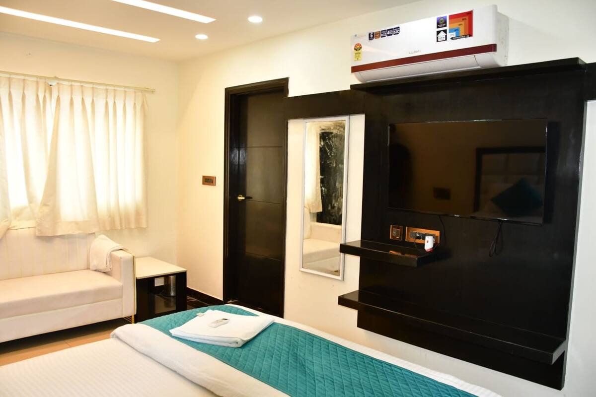 A hotel room with a bed, a sofa, a small table, a mirror, and a TV.