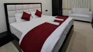 A modern hotel room with a large bed, a white sofa, and a ceiling fan. - Hotel MKG Inn Club and Bar Jaipur (Jaipur)