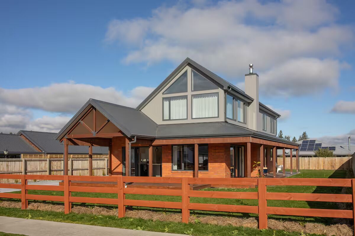 A modern two-story house with a large front porch, a covered outdoor seating area, and a fenced backyard.