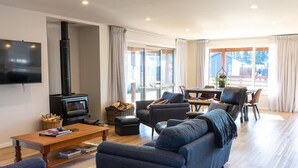 A modern living room with a fireplace, comfortable seating, a flat-screen TV, and a dining area with natural light.