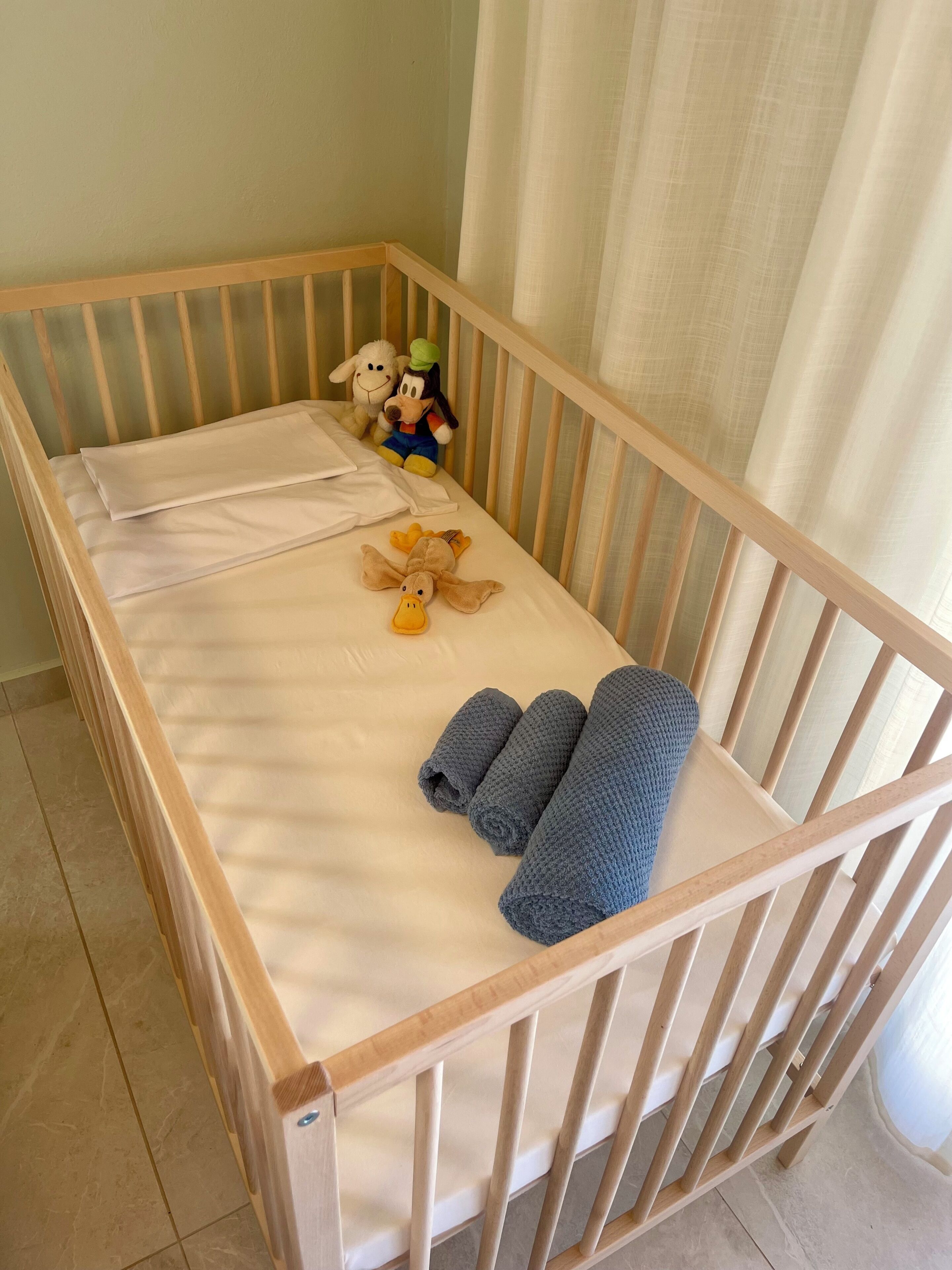 Een reisbedje met een witte matras, een zacht speeltje en opgerolde handdoeken.