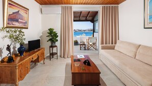 A living room with a wooden ceiling, a sofa, a coffee table, a TV, and a view of the sea through a glass door. - Art Sounion, Seafront Elegance (Sounion, Lavreotiki)