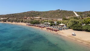 A beach with clear turquoise water, a sandy shore, and a row of beach umbrellas and sun loungers. - Art Sounion, Seafront Elegance (Sounion, Lavreotiki)