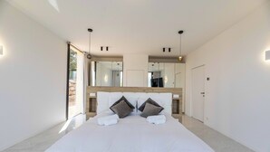 Een moderne slaapkamer met een groot bed, twee nachtkastjes, een spiegel en een deur.