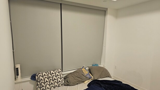 Ein Schlafzimmer mit einem Bett, Kissen, einer Decke und einem Fenster mit Jalousien.