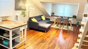 Een moderne woonruimte met een eethoek, een bank met kussens, een eettafel met stoelen en een trap.