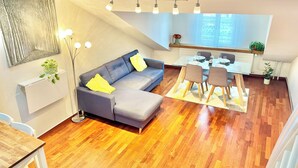 Een moderne woonkamer met een grijze bank, een eettafel met stoelen en een keuken op de achtergrond.