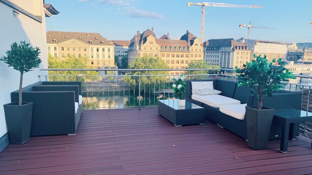Een terras op het dak met rieten meubels, een glazen tafel en potplanten.