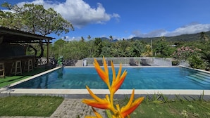 A swimming pool with a waterfall feature, surrounded by lush greenery and a clear blue sky. - Eco Moringa Garden (Bali)