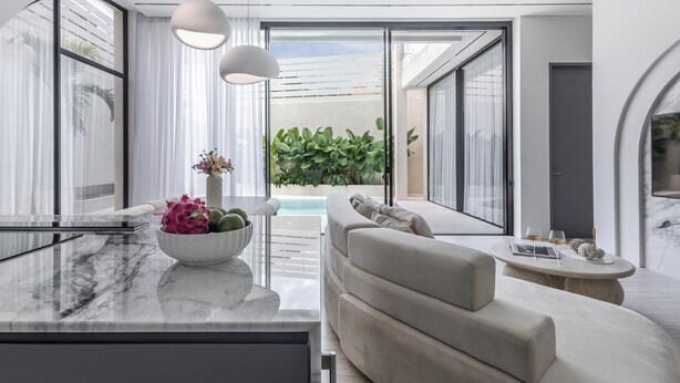 Una sala de estar moderna con cubierta de mármol, un sofá color beige y una zona de comedor con una mesa redonda.
