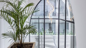 Un interior moderno con una planta grande en maceta, una estructura de vidrio y una lámpara colgante.
