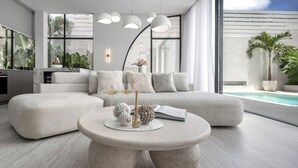 Una sala moderna con un amplio sofá seccional, una mesa de centro redonda con objetos decorativos, y vista a una piscina.