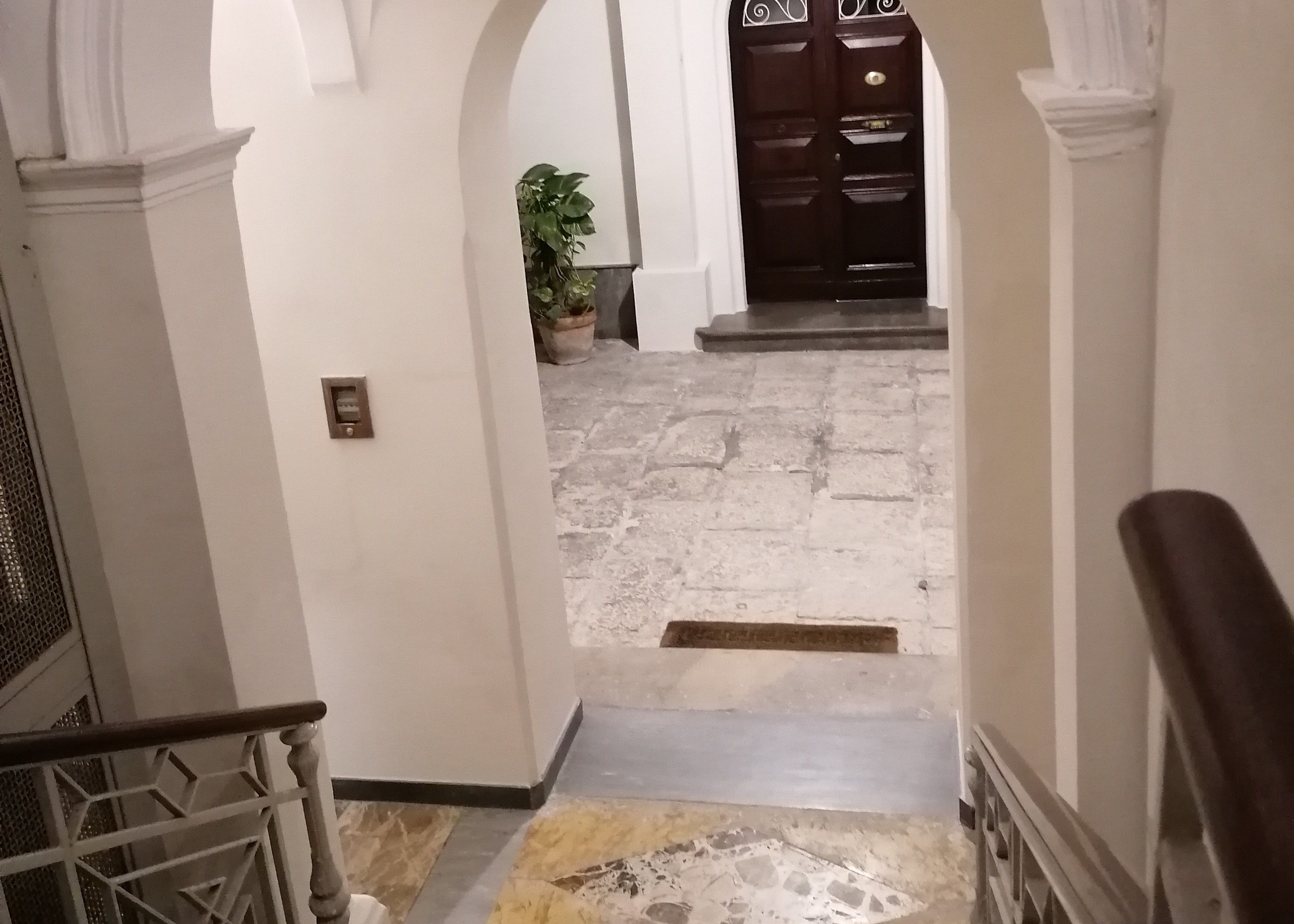 A hallway with a stone floor, white walls, and a dark wooden door at the end.