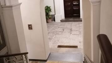 A hallway with a stone floor, white walls, and a dark wooden door at the end.