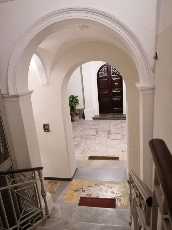 A hallway with an arched doorway leading to a room with a dark wooden door. - BelliniStay - In the city center, just a stone's throw from the sea. (Trapani)