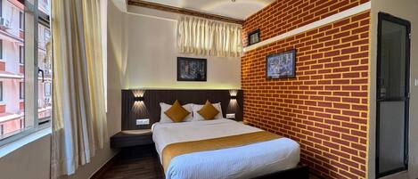 Una habitación de hotel con pared de ladrillo decorativa, una cama grande con cabecera, una mesita de noche y una ventana con cortinas.