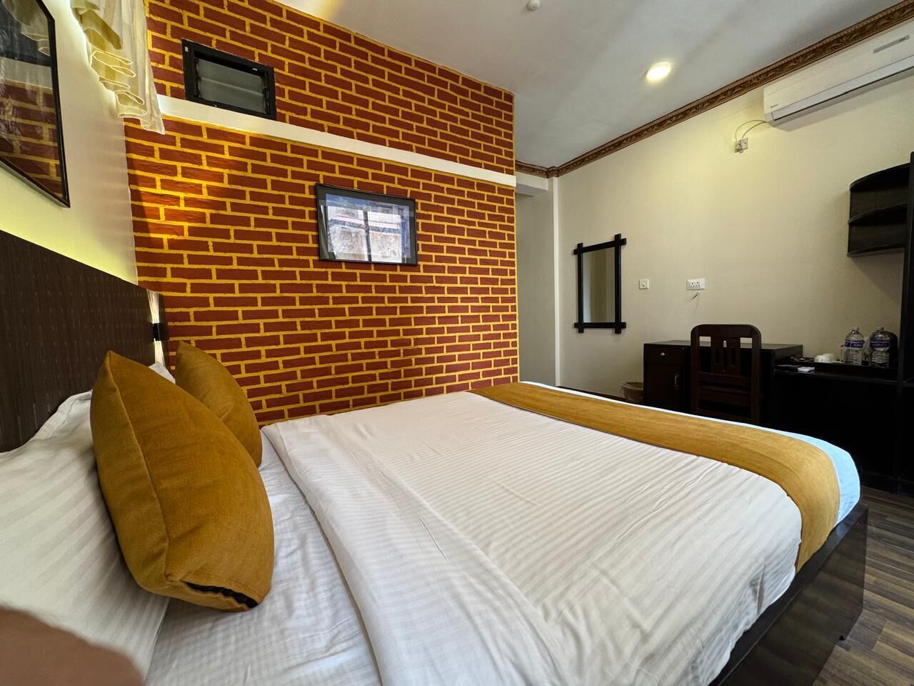 A hotel room with two beds, a brick accent wall, a desk, and a television.