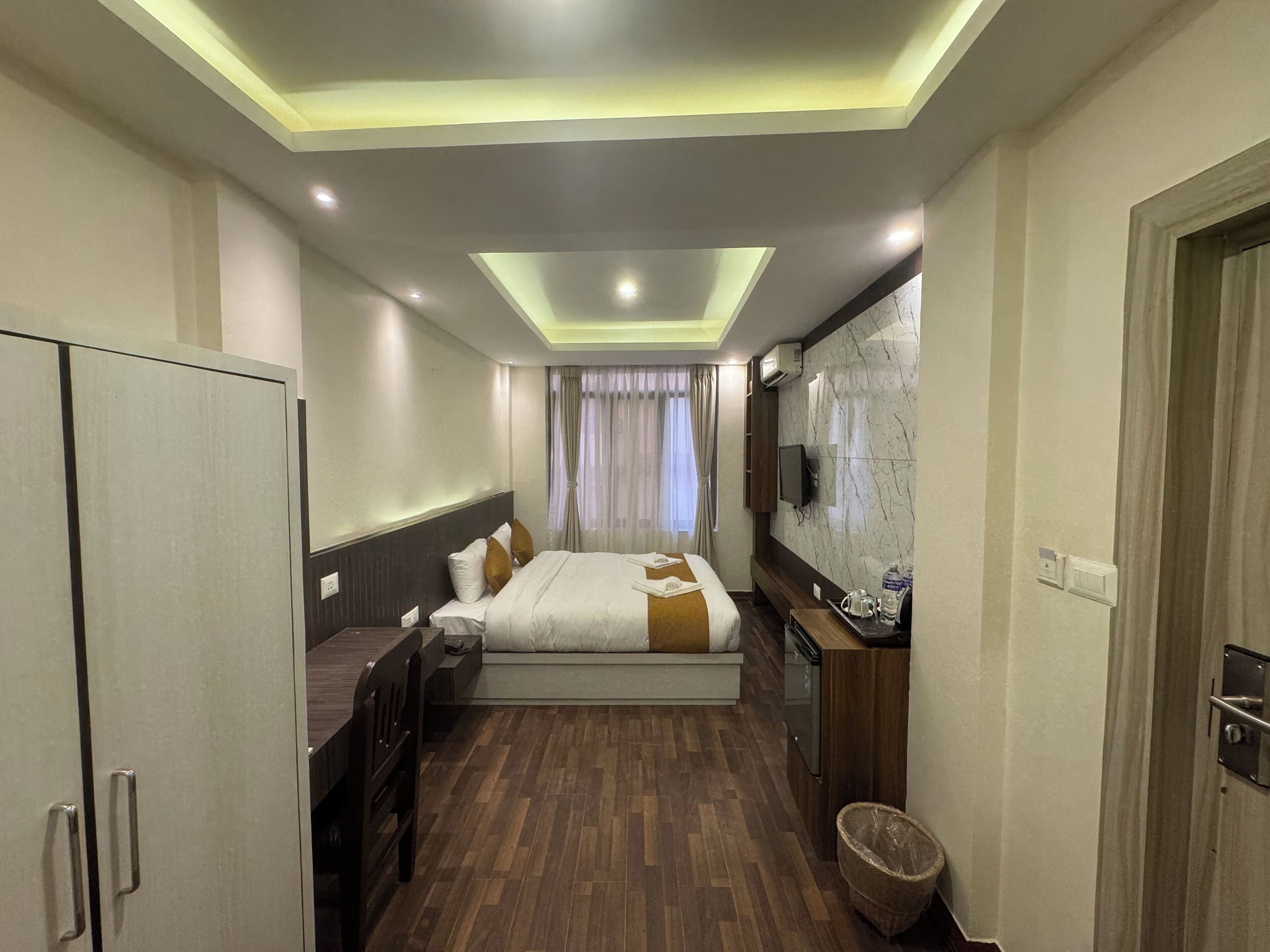 A hotel room with a bed, a desk, a TV, and a minibar.