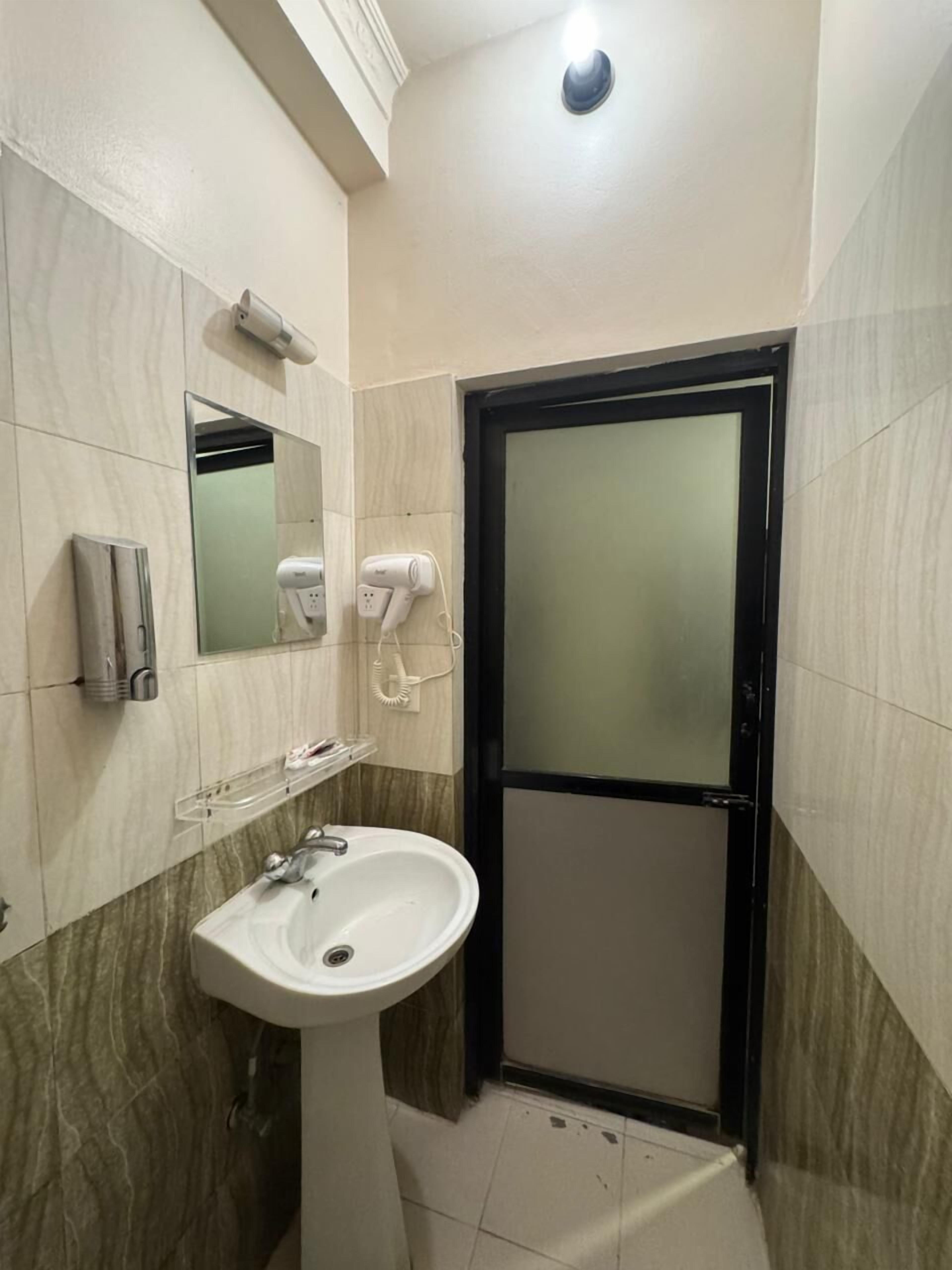 A bathroom with a white sink, a mirror, a hairdryer, and a towel dispenser.