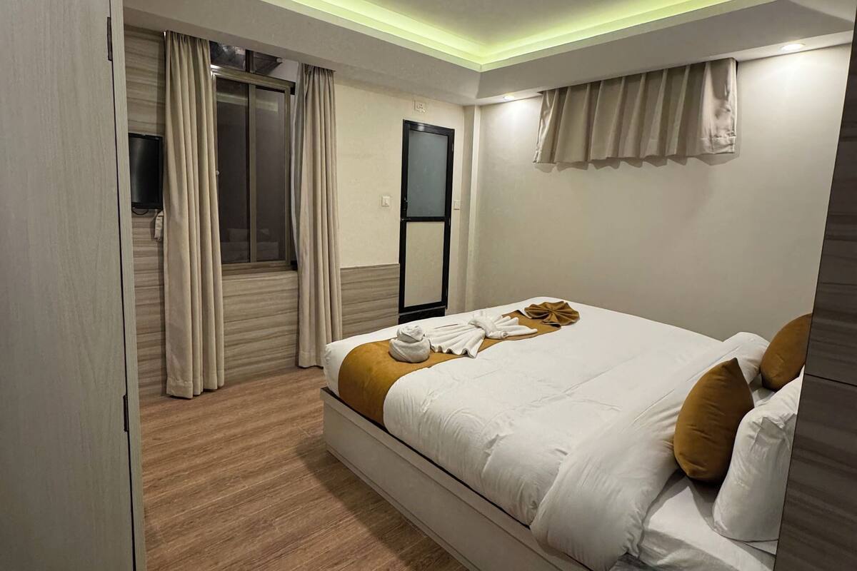 Een moderne hotelkamer met een groot bed, een houten vloer, een flatscreen televisie en een schuifdeur naar een balkon.