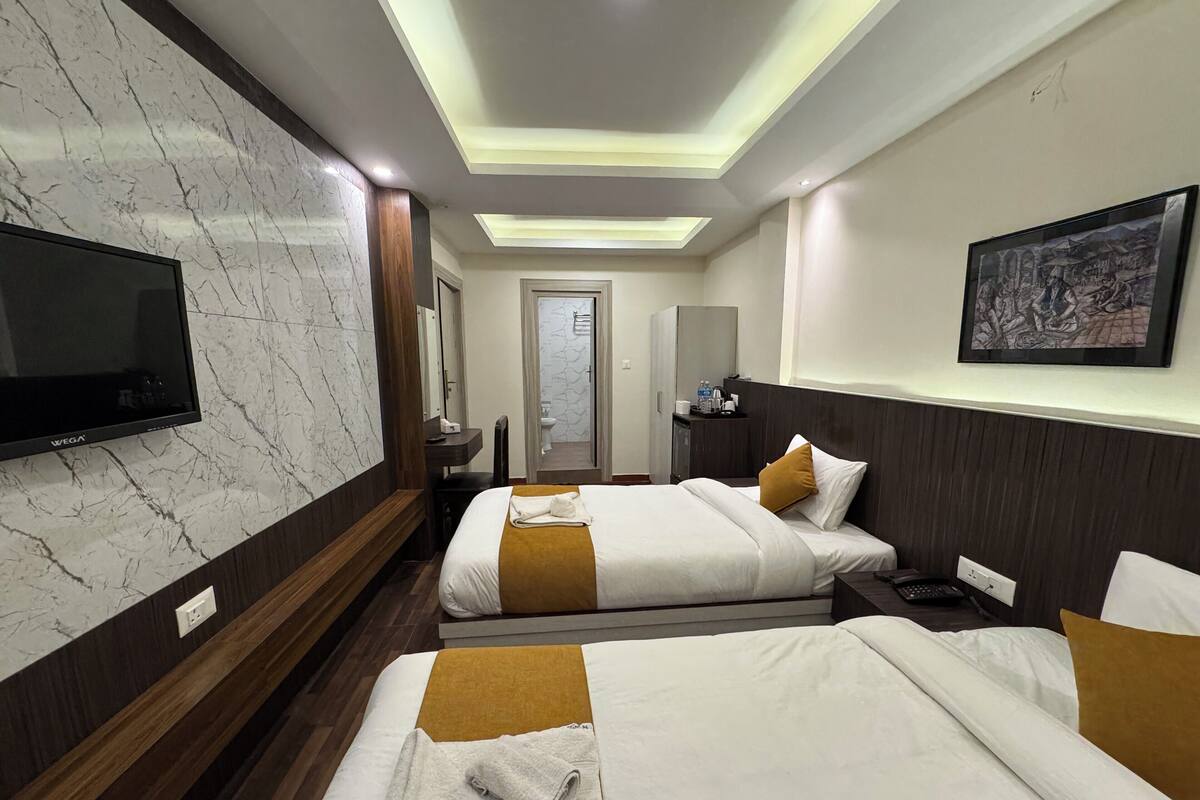 Een hotelkamer met twee bedden, een televisie, een badkamer en een schilderij aan de muur.