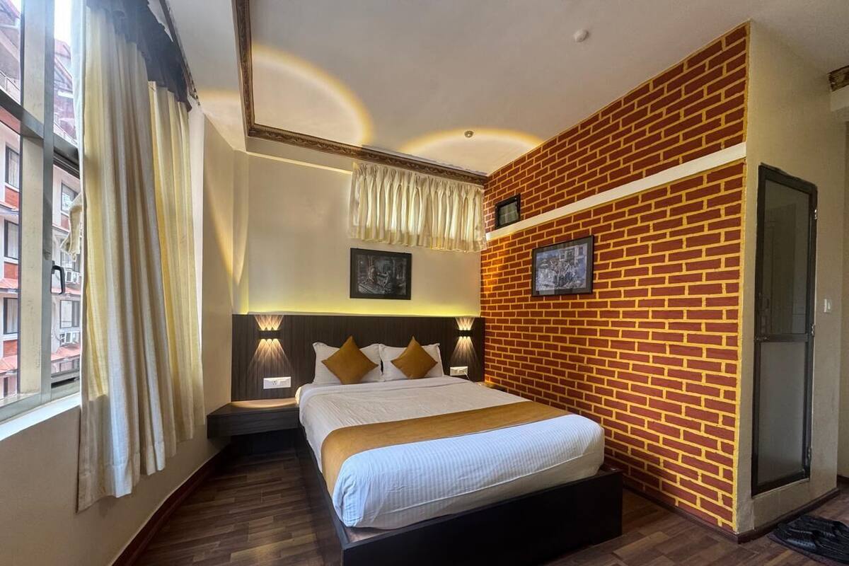 Een hotelkamer met een groot bed, een wand van baksteen, een schuifdeur en uitzicht op de stad door het raam.