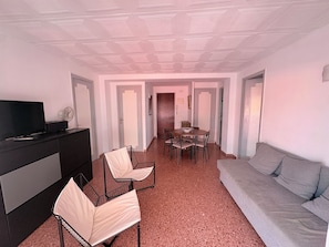 Una sala de estar con sofá, televisor, mesa de comedor con sillas y una zona de kitchenette.
