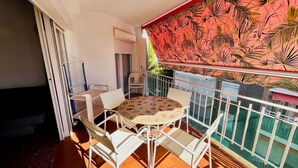 Un balcón con una mesa y sillas, una pared de diseño rojo y una cerca de malla verde.