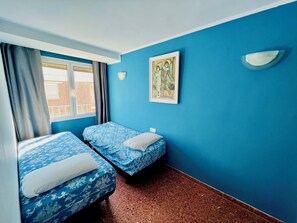 A room with two beds, a window with curtains, a wall-mounted light, and a framed picture. - Salou | 5 pers | Swimming pool | Beach & PortAventura (Salou)