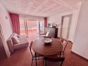 Una habitación con una mesa redonda de madera, un sofá, un televisor y un balcón con vistas.