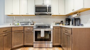 Une cuisine avec des armoires blanches, des appareils en acier inoxydable et un plancher en bois.
