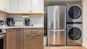 Une cuisine avec des meubles blancs, un réfrigérateur en acier inoxydable, une machine à café et un lave-linge.