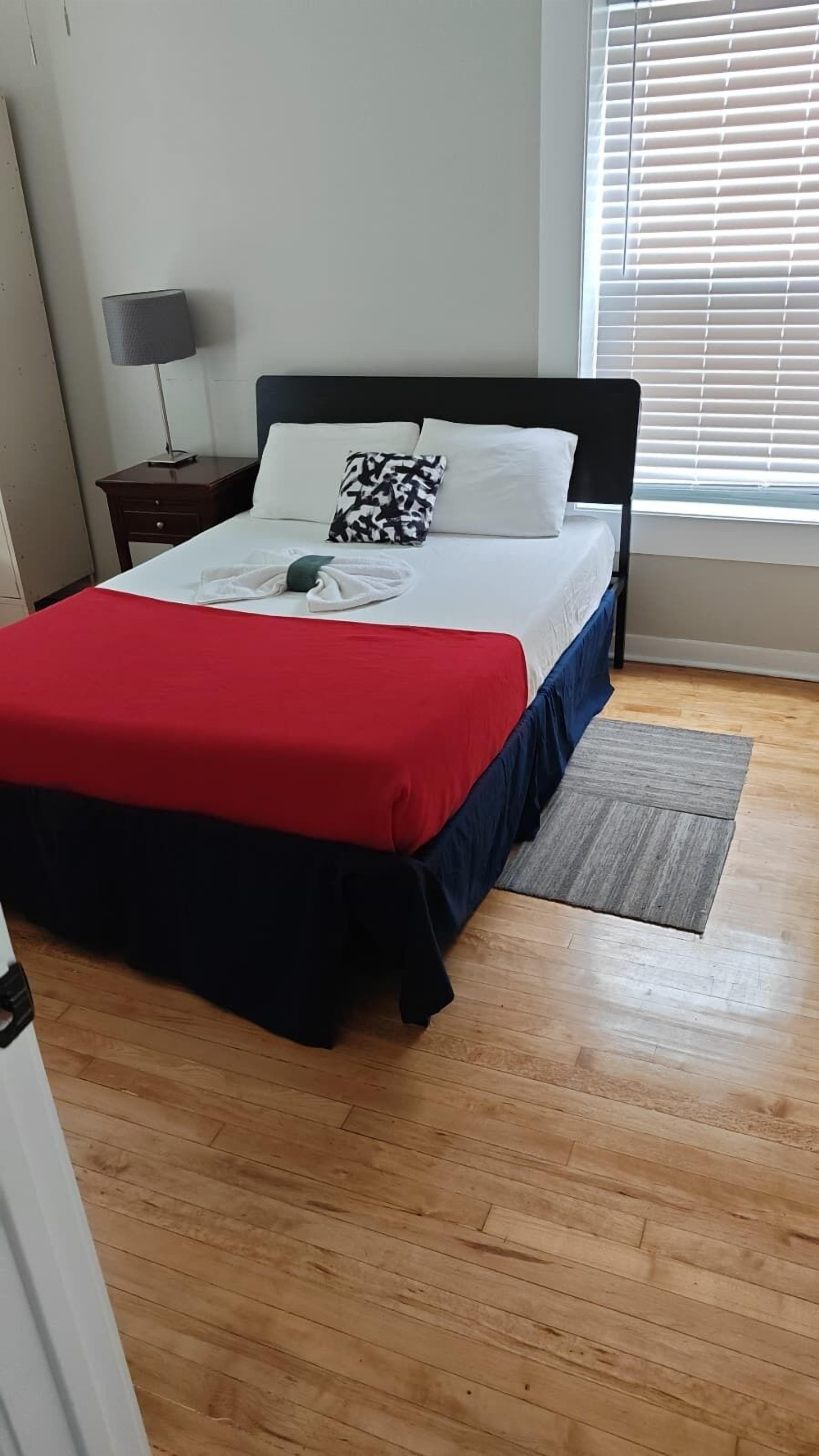 Un dormitorio con cama, mesita de noche, lámpara y ventana con persianas.