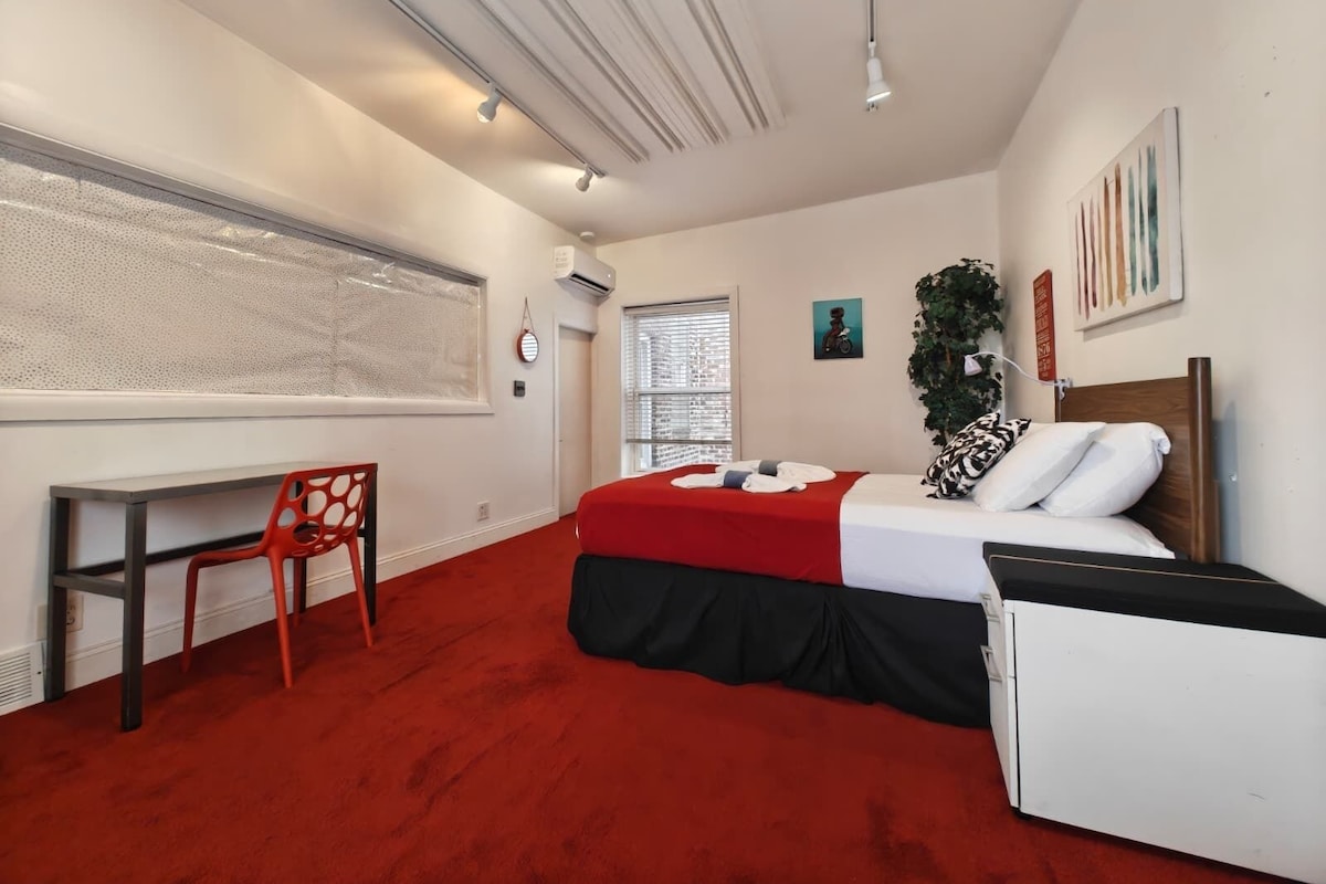A bedroom with a bed, a desk, a chair, a window, and a wall-mounted air conditioner.