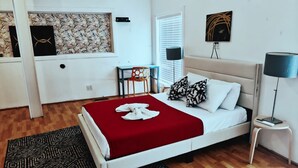 A bedroom with a bed, a desk, a chair, a lamp, and a wall with artwork. - Grand House (Chicago)