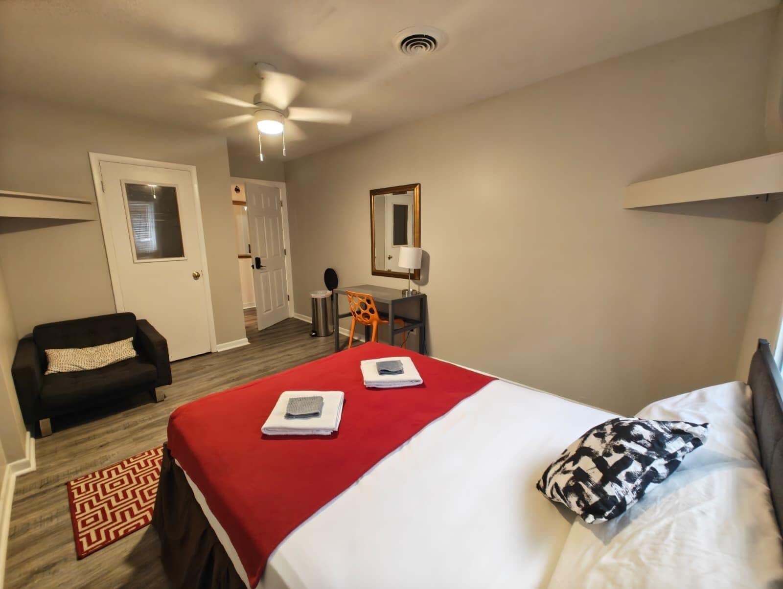 Una habitación de hotel con cama, escritorio, silla, ventilador de techo y puerta.