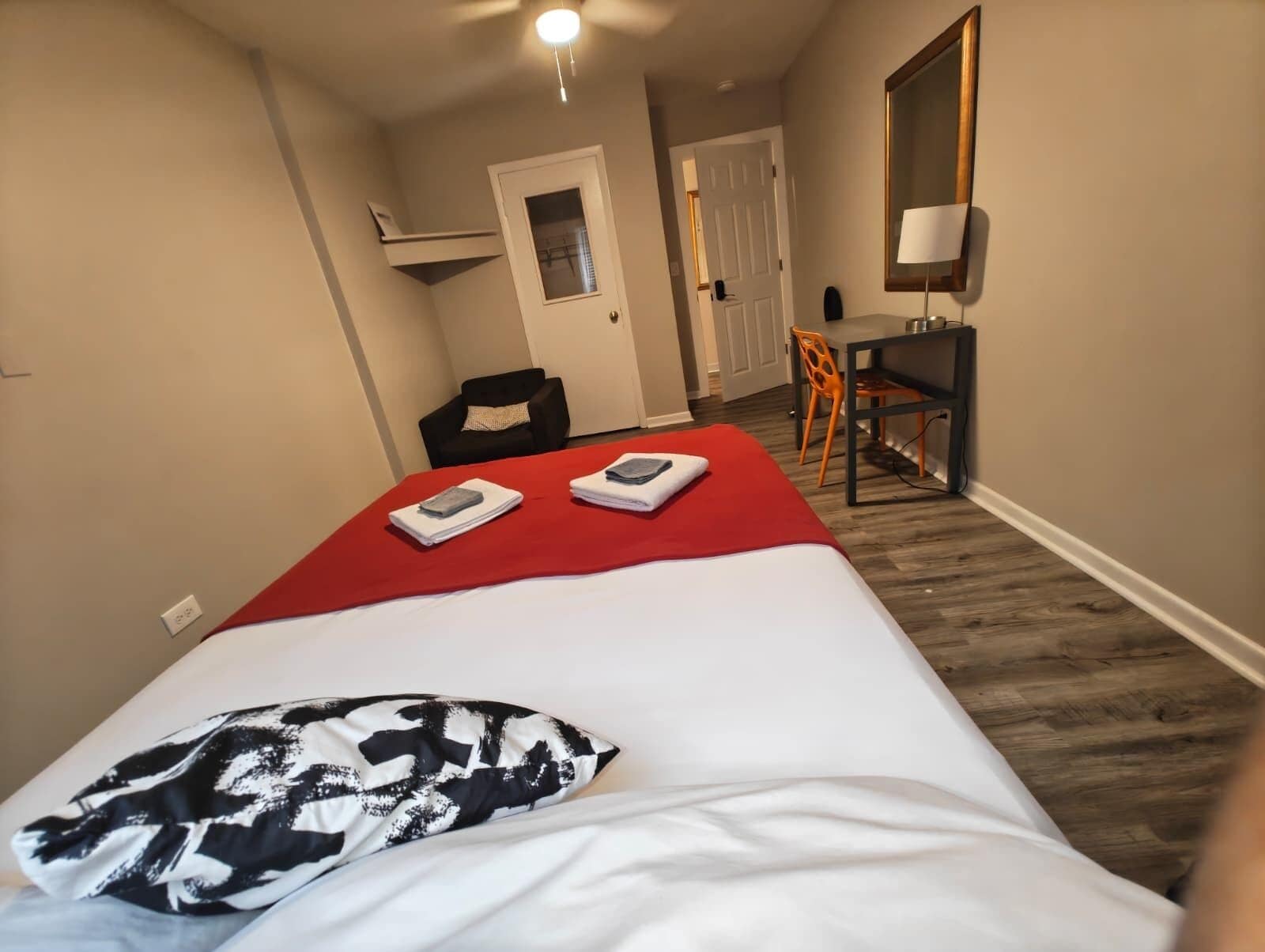 A hotel room with a bed, a desk, a chair, a mirror, and a door.
