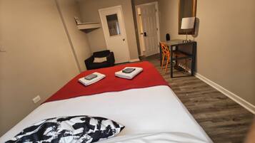 A hotel room with a bed, a desk, a chair, a mirror, and a door.