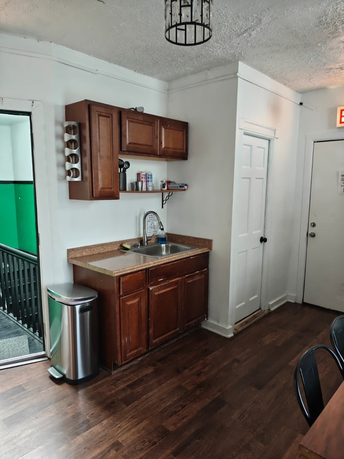 A compact kitchen with wooden cabinets, a stainless steel sink, and a trash can.