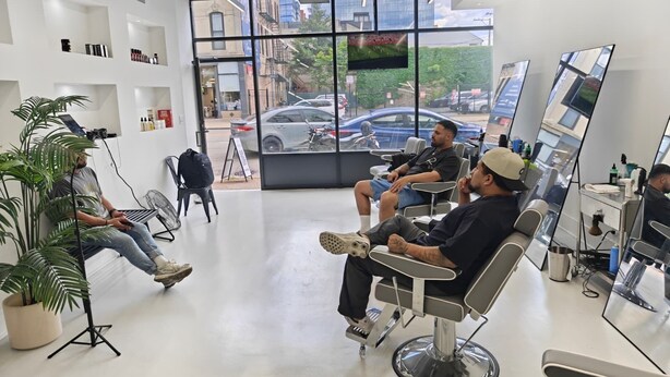 A modern salon interior with multiple seating areas, a large window with a view of the street, and a plant in the foreground. - Grand House (Chicago)