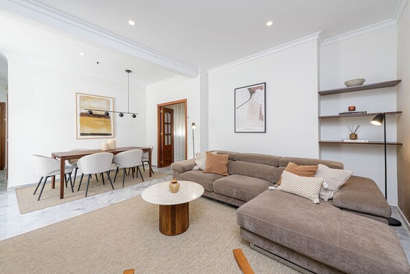 A spacious living room with a large sectional sofa, a dining area with a table and chairs, and a minimalist decor style.