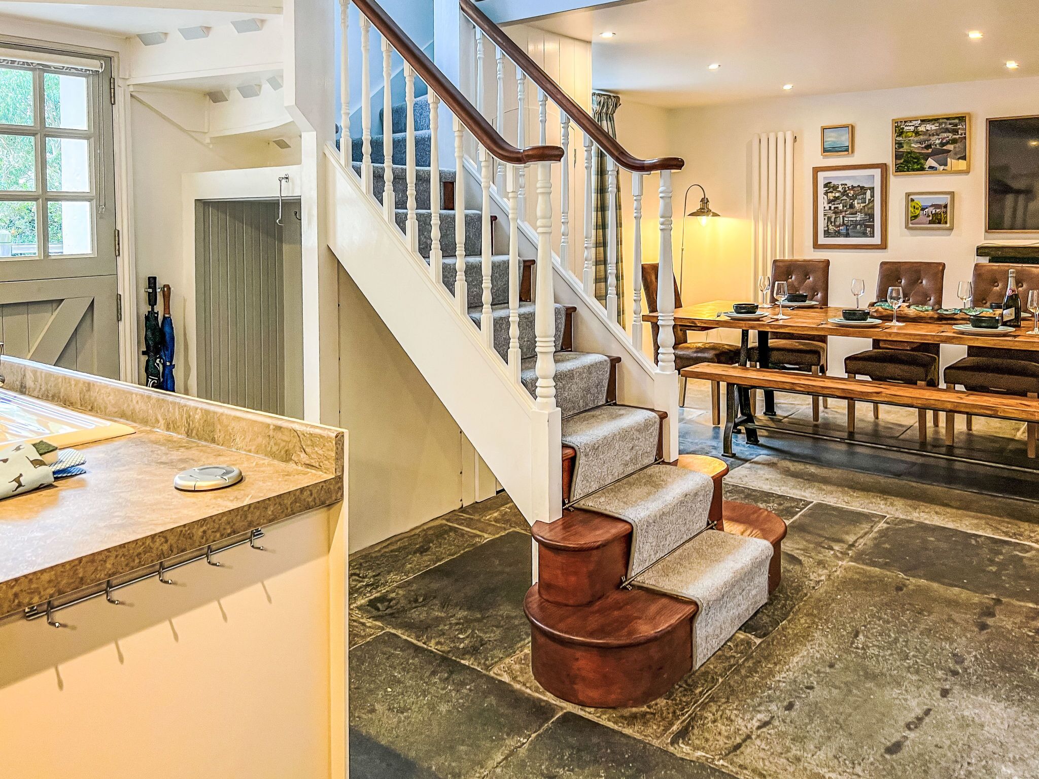 A spacious living area with a staircase, a dining table set for six, and a large window.
